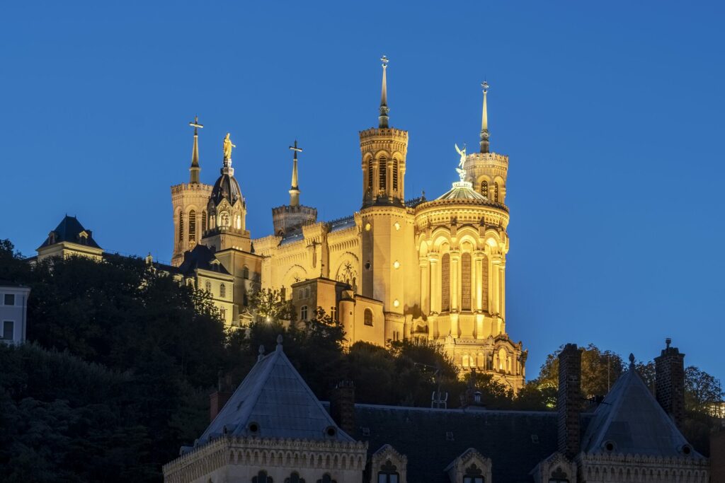 La basilique Notre-Dame de Fourvière illuminée à la tombée de la nuit, au-dessus des toits de Lyon
