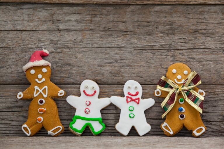 Quatre biscuits en forme de personnages, deux en pain d'épices décorés et deux glaçages blancs, alignés devant un mur de planches de bois