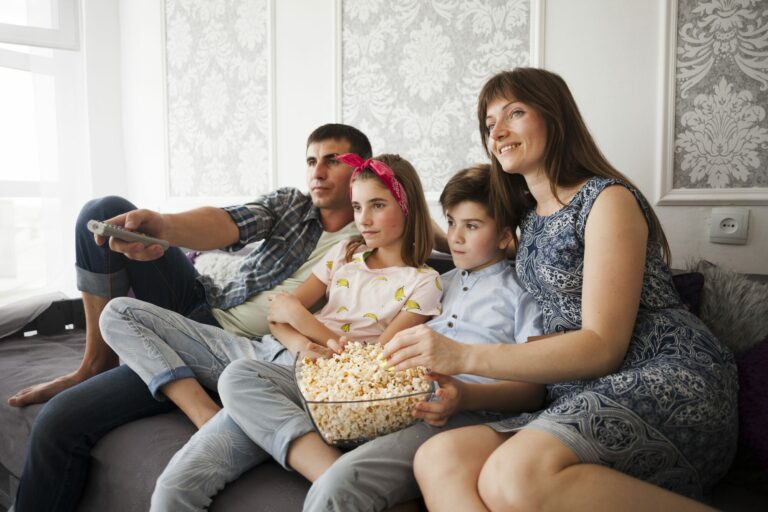 Famille réunie sur un canapé devant la télévision, partageant un saladier de pop-corn dans le salon