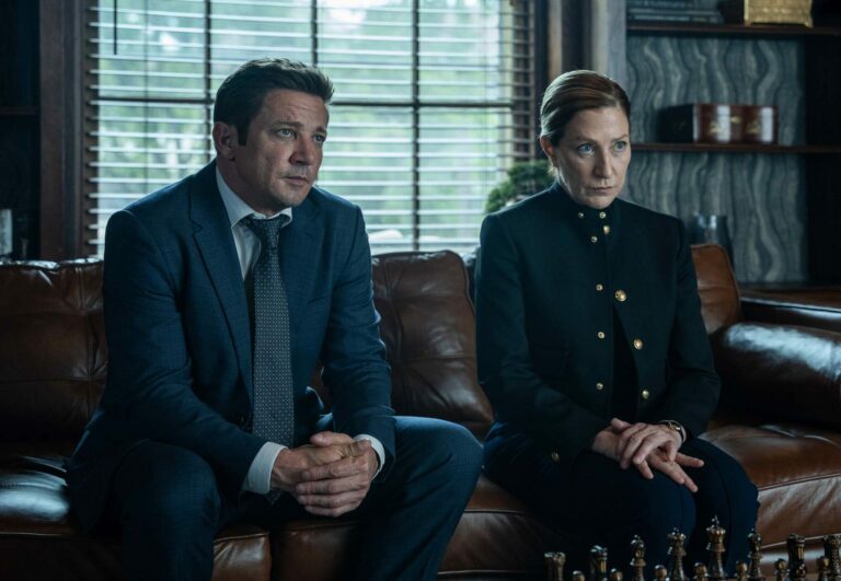 Jeremy Renner et Edie Falco assis sur un canapé en cuir dans la saison 5 de la série Mayor of Kingstown