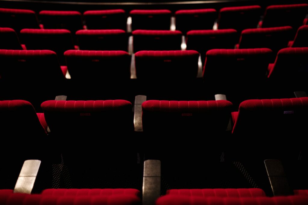 Rangées de fauteuils rouges vides dans une salle de spectacle plongée dans la pénombre