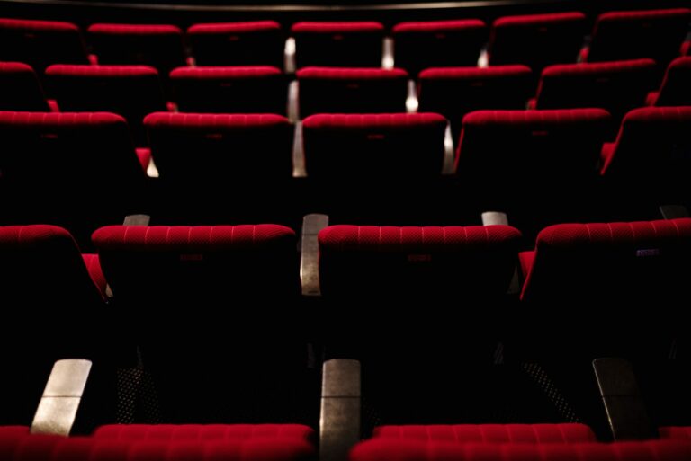 Rangées de fauteuils rouges vides dans une salle de spectacle plongée dans la pénombre