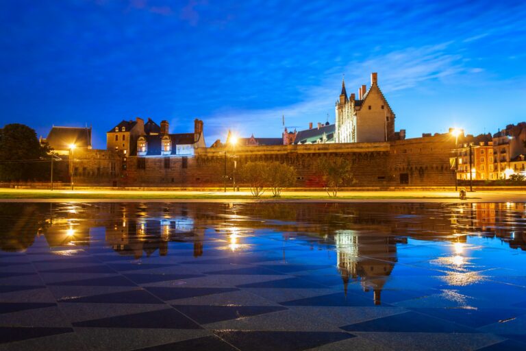 Le château des ducs de Bretagne illuminé à la tombée de la nuit, avec son reflet dans l’eau, à Nantes