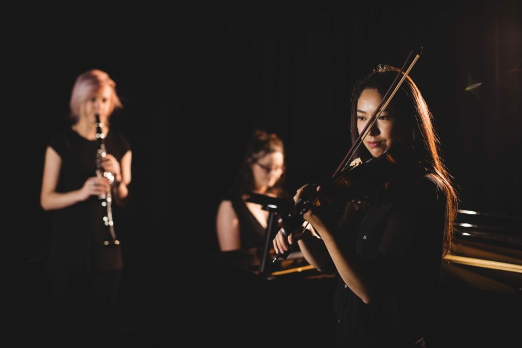 Trois jeunes musiciennes jouant de la flûte et du violon sur fond sombre