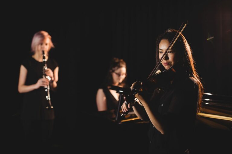 Trois jeunes musiciennes jouant de la flûte et du violon sur fond sombre