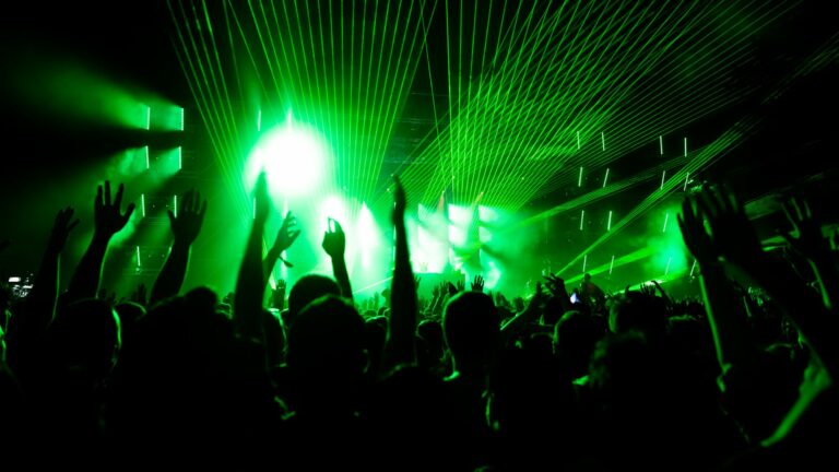 Silhouettes d'un public bras levés devant une scène balayée de faisceaux laser verts lors d'un concert