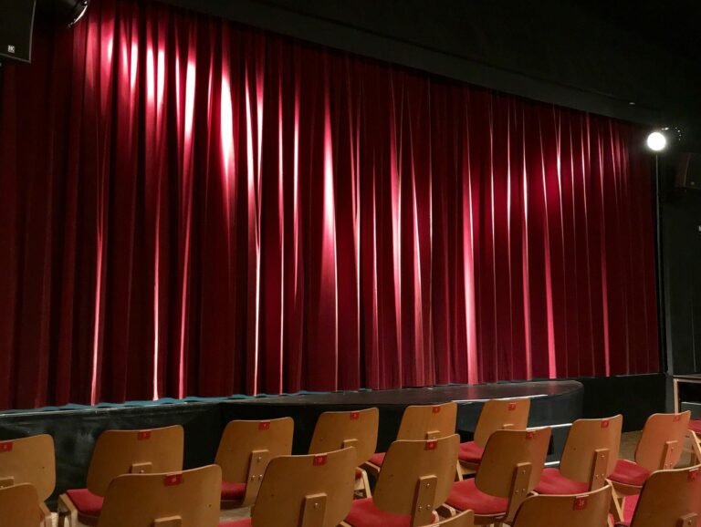 Salle de théâtre vide avec ses fauteuils face à une scène fermée par un grand rideau rouge
