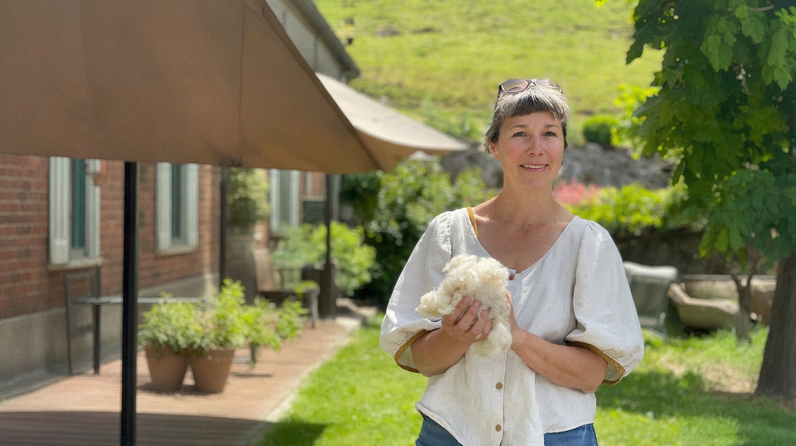 Gaëlle Cornelis tenant une toison de cachemire dans son jardin, format paysage