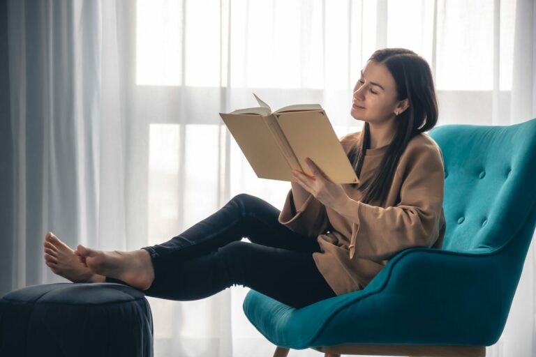 Jeune femme lisant un livre dans un fauteuil près d’une fenêtre