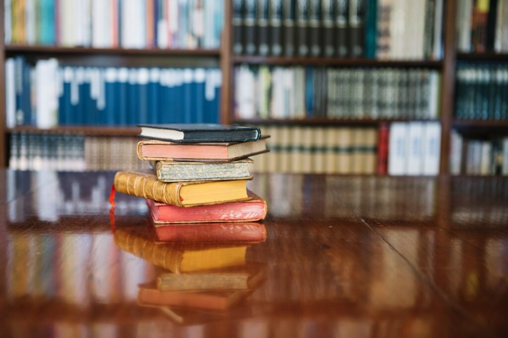 Pile de livres anciens posée sur une table de bibliothèque, devant des rayonnages flous
