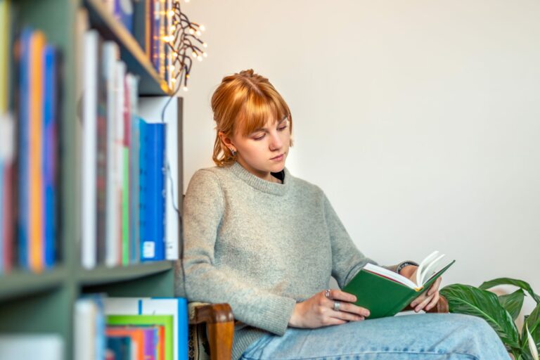 Jeune femme rousse plongée dans un livre, assise entre des rayonnages de librairie