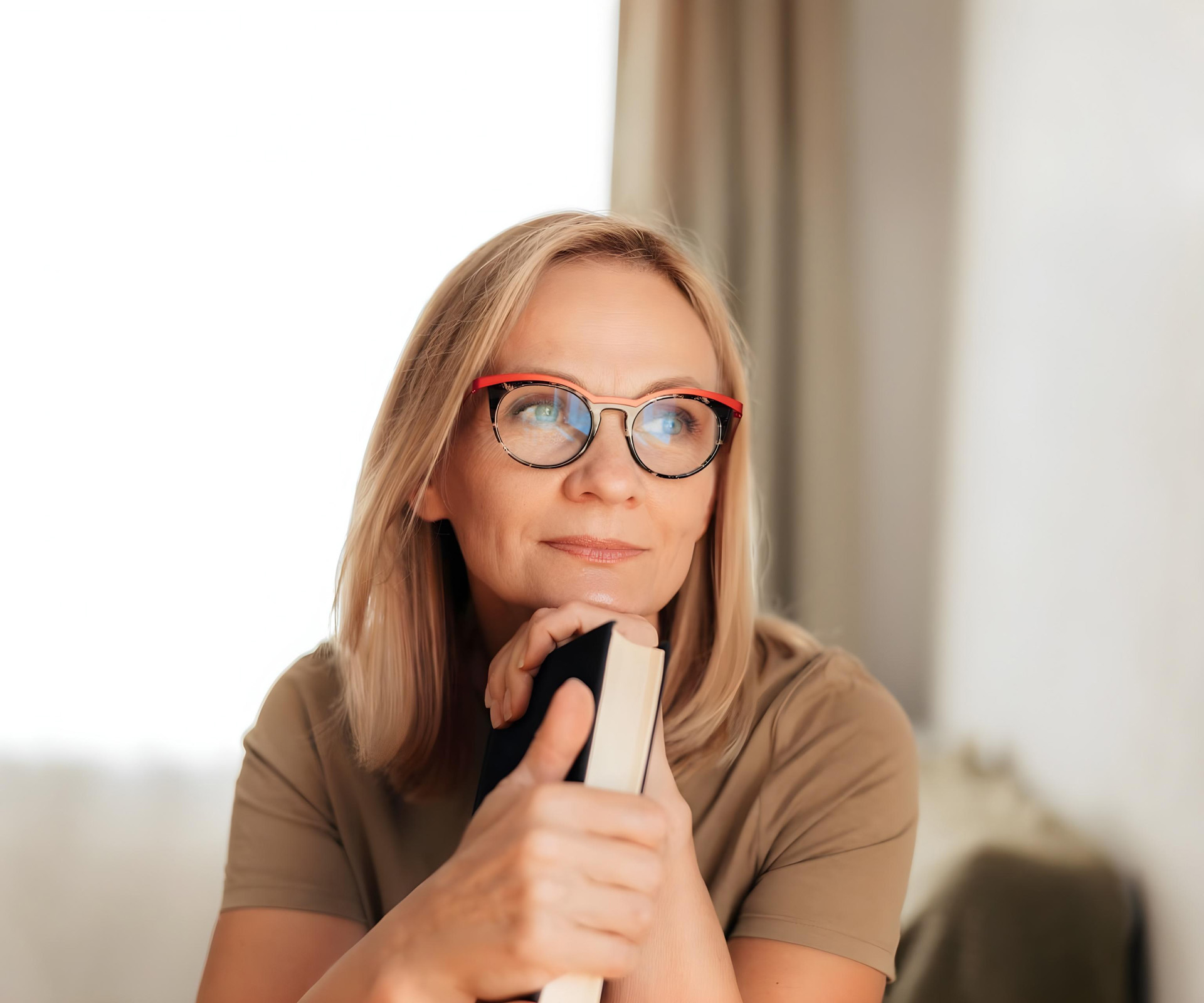 Femme blonde à lunettes, pensive, serrant un livre contre son menton