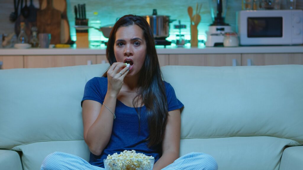 Femme captivée par un film à suspense, un bol de pop-corn à la main dans son canapé