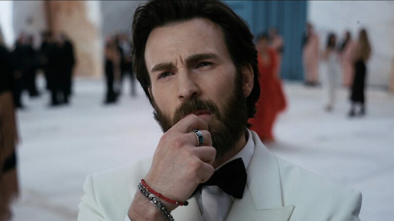 Chris Evans en smoking blanc, la main au menton, lors d’un gala dans le film Sacrifice de Romain Gavras