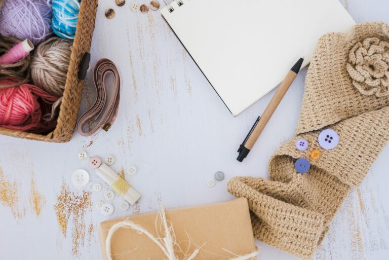 Vue du dessus de pelotes de laine colorées dans un panier, d’un carnet, d’un crayon et d’un mètre ruban sur un bureau en bois