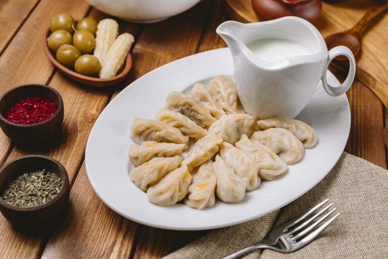 Assiette de raviolis en forme de croissant servis avec un pot de yaourt, des bols de sumac et d'herbes séchées et une coupelle d'olives sur une table en bois