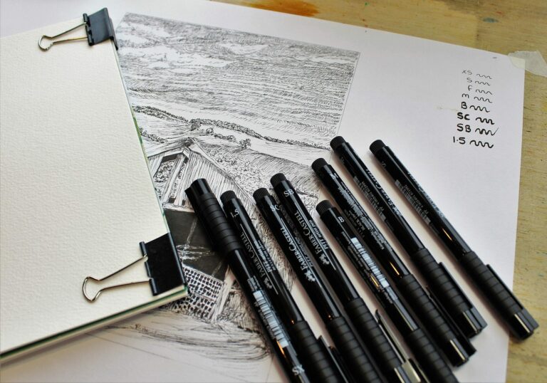Feutres et stylos à encre noire posés sur un carnet de croquis dessiné à l'encre