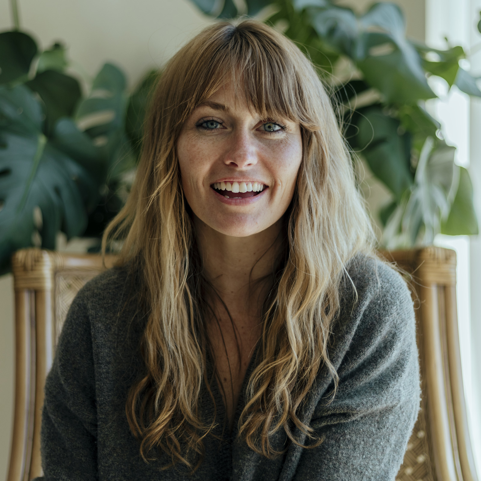 Femme souriante aux cheveux longs dans un fauteuil, entourée de plantes