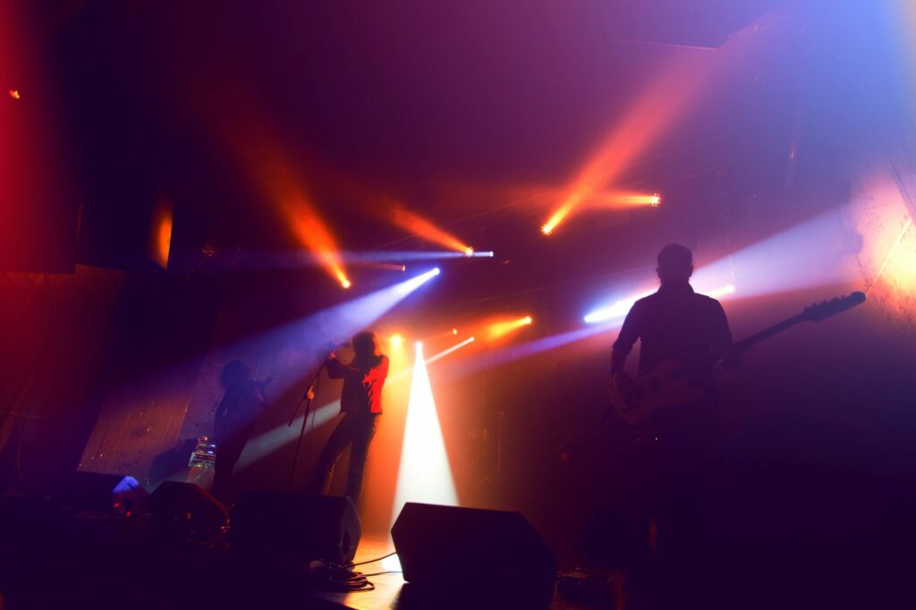Silhouettes de musiciens sur une scène de concert baignée de projecteurs rouges et bleus dans la fumée