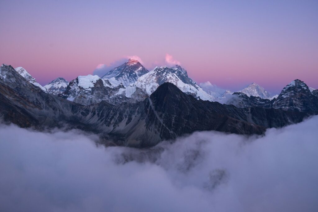 Le sommet enneigé de l'Everest et les crêtes de l'Himalaya au-dessus d'une mer de nuages, sous un ciel rosé au crépuscule