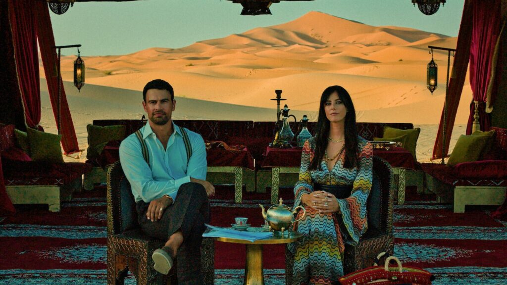 Un homme et une femme assis sous une tente richement décorée, face aux dunes du désert, dans la série The Gentlemen