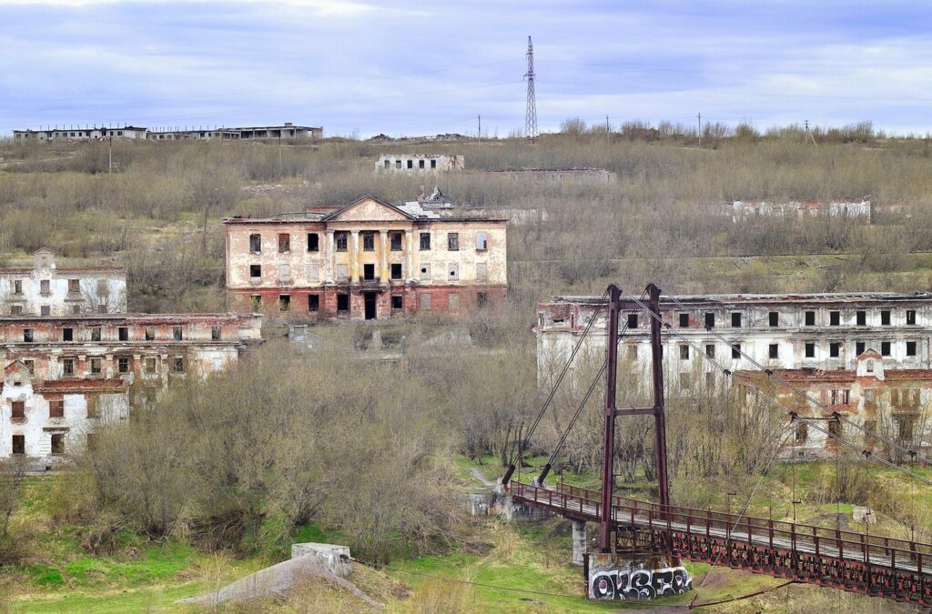 Immeubles abandonnés et en ruine sur une colline envahie par la végétation, sous un ciel gris