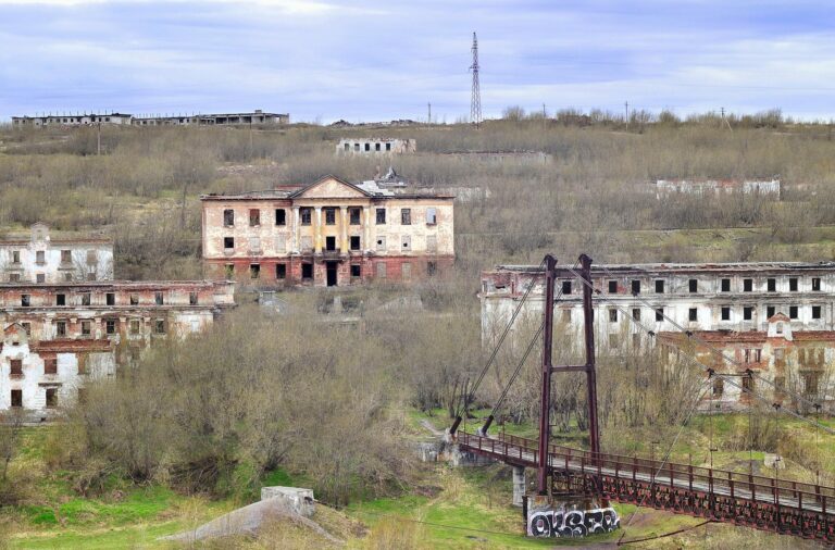 Immeubles abandonnés et en ruine sur une colline envahie par la végétation, sous un ciel gris
