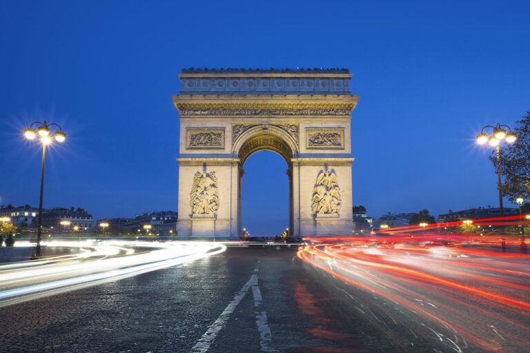 L’Arc de Triomphe illuminé la nuit, entouré de traînées lumineuses laissées par les voitures, à Paris