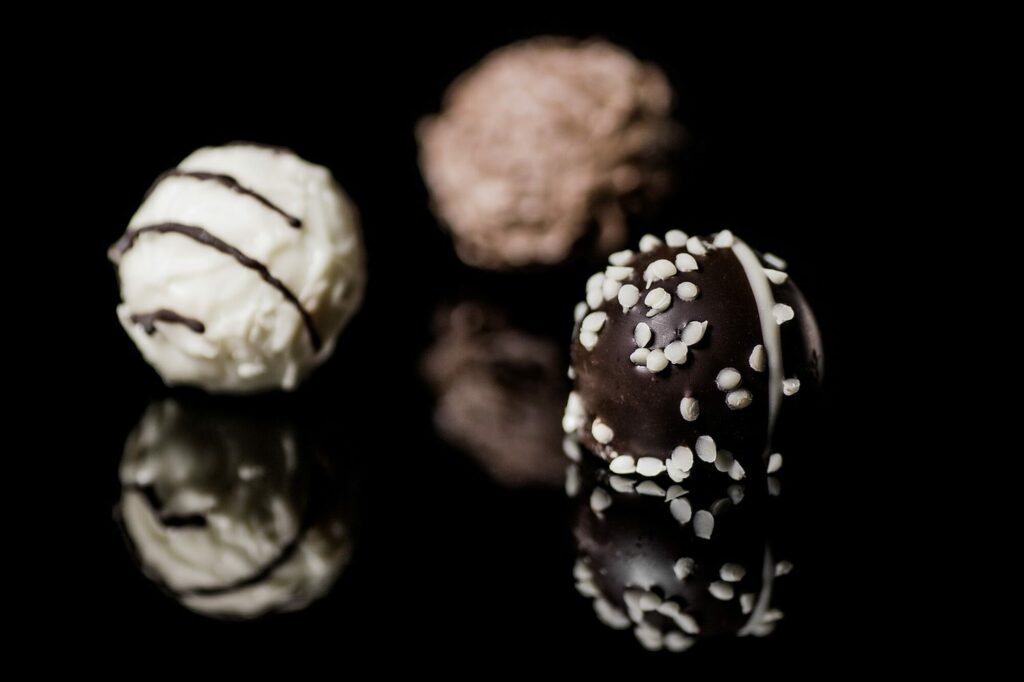 Trois bonbons de chocolat ronds, blanc, au lait et noir décoré, posés sur une surface noire brillante