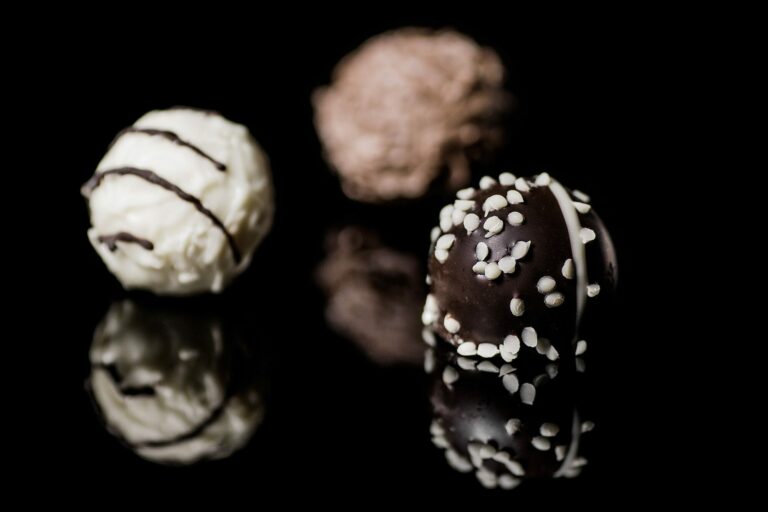 Trois bonbons de chocolat ronds, blanc, au lait et noir décoré, posés sur une surface noire brillante