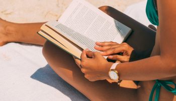 Close-up of a woman reading on a sandy beach in summer sunlight.