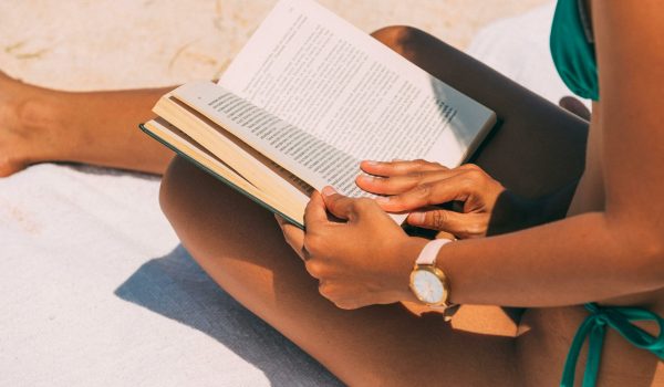 Close-up of a woman reading on a sandy beach in summer sunlight.