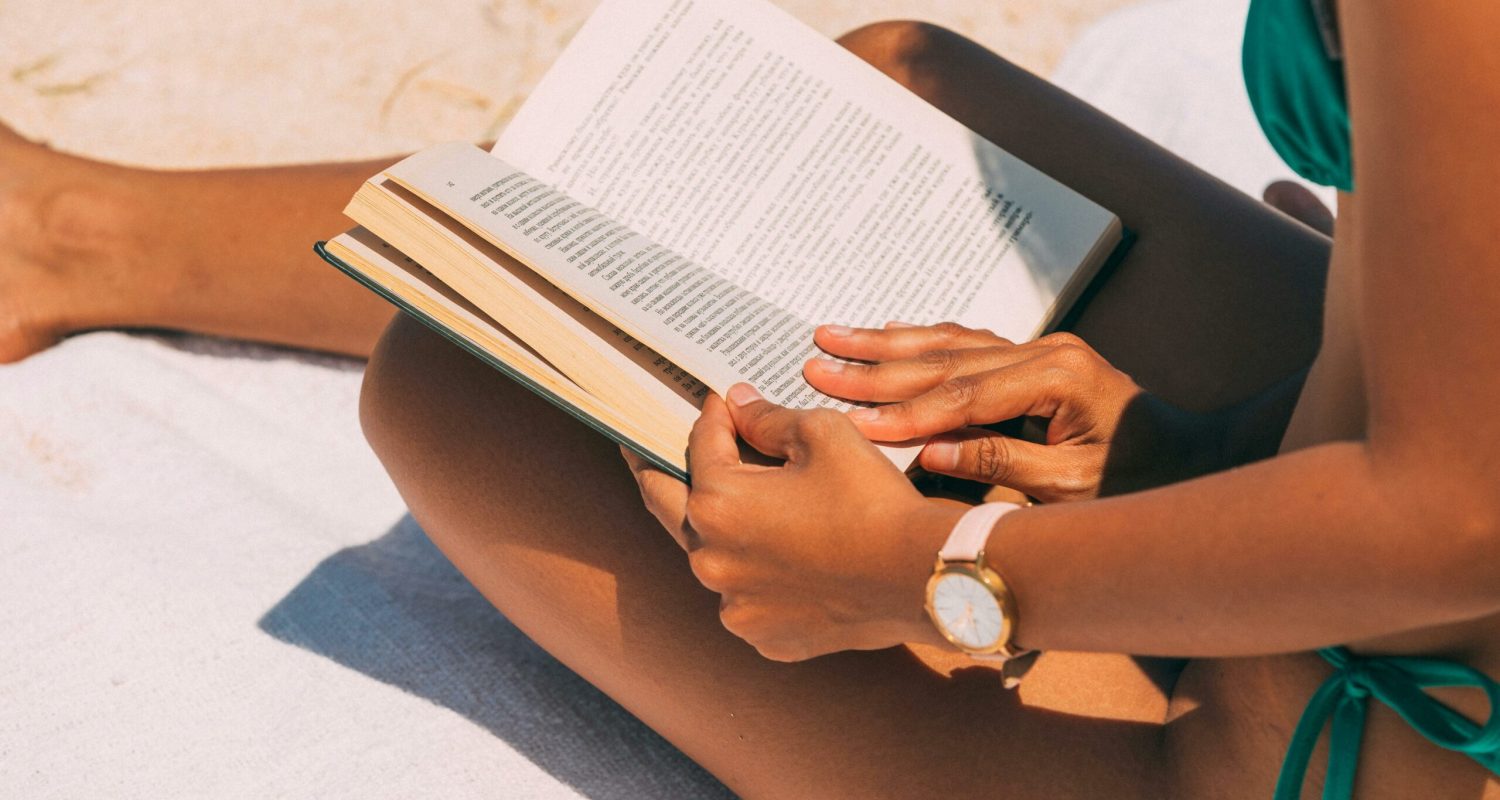 Close-up of a woman reading on a sandy beach in summer sunlight.